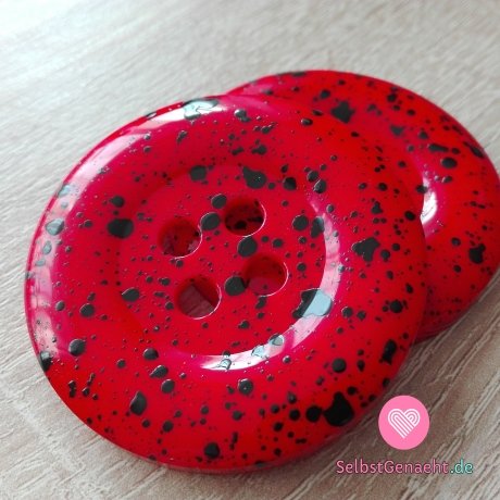 Mega großer roter Knopf mit schwarzen Spritzern